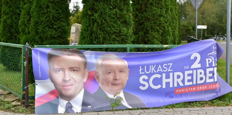 Zdjęcie wykonane we wtorek, 2 października. Baner promujący jednego z kandydatów Prawa i Sprawiedliwości zawieszony na ogrodzeniu miejsca pamięci w Drożdzienicy. W tle pomnik upamiętniający pomordowanych i poległych w latach 1939-1945.